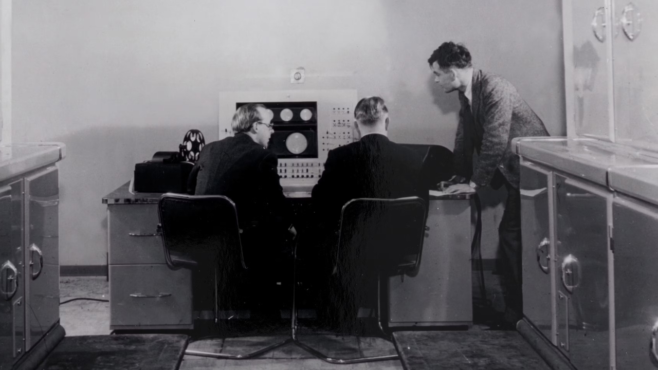 Three people gathered around an early computer